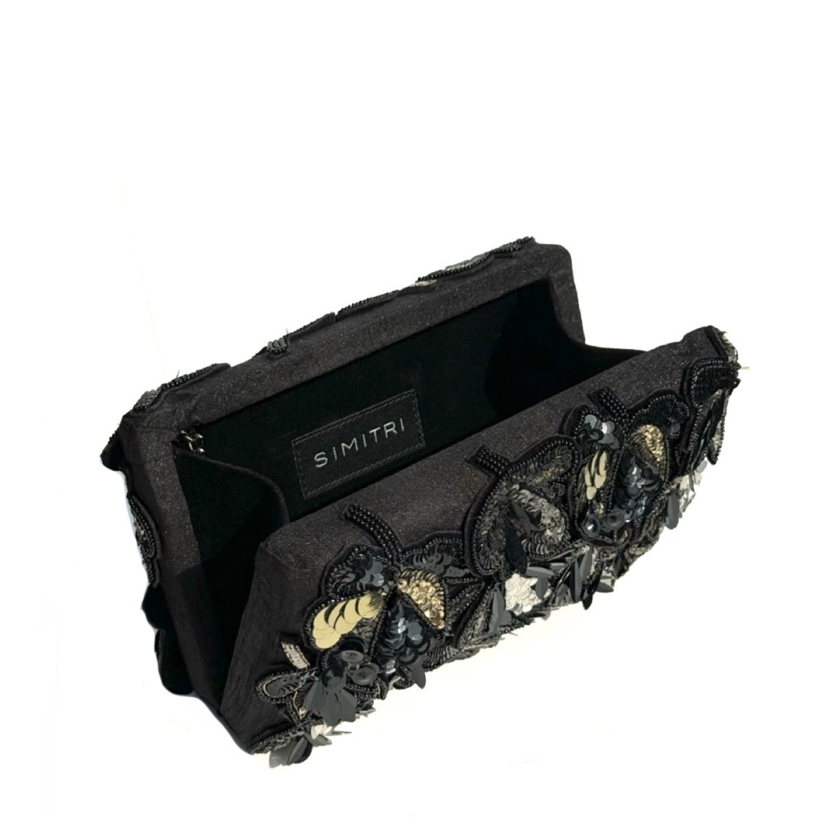 A black fabric clutch bag with intricate black lace appliques, 3D floral embellishments, and gold glitter accents, shown open on a white background. The brand name 'SIMITRI' is visible on a black label inside the pouch.